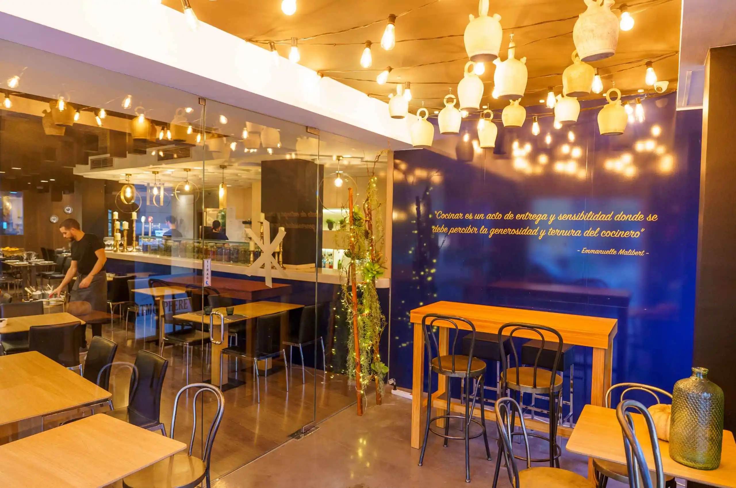 Fotografía del restaurante francés, con iluminación cálida y al fondo un texto en letras doradas sobre fondo azul. El texto es una declaración sobre la pasión por la cocina de la chef.